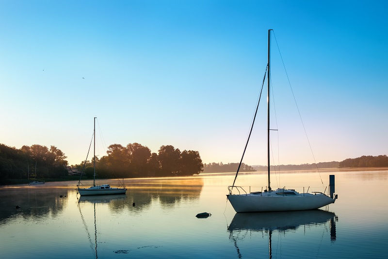 Yachts float on the calm waters of the lake. Early morning. Masuria, Poland .